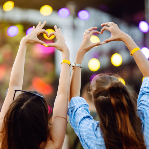 Two women at a concert making heart shapes with their hands